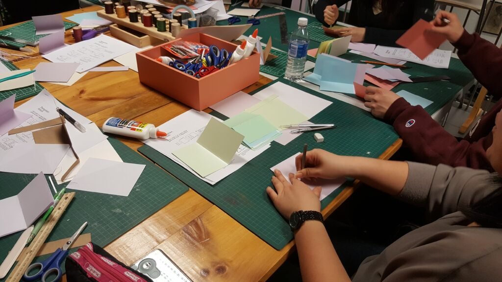 Students assembling handmade small books for bookbinding class.