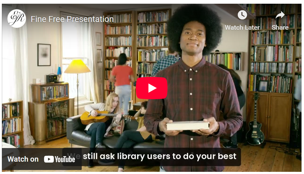 The Fine Free Presentation video thumbnail on Youtube shows a student holding a book and smiling at a screen in a room full of books.