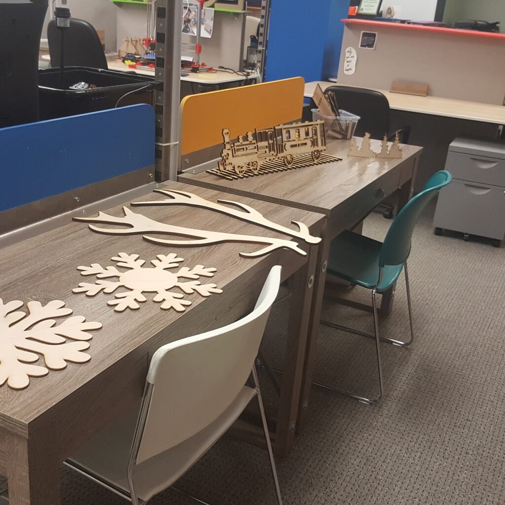 A series of winter-themed laser cut items on display: giant snowflakes, deer antlers, train on a railway with pine trees.